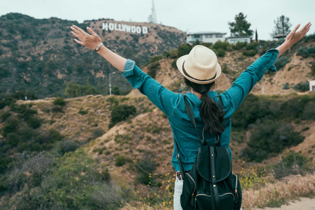 Woman standing in front of Hollywood sign with arms raised