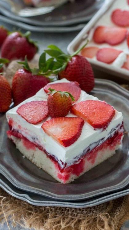 picture of sliced strawberry poke cake filled with whipped cream and topped with sliced strawberries on a silver plate