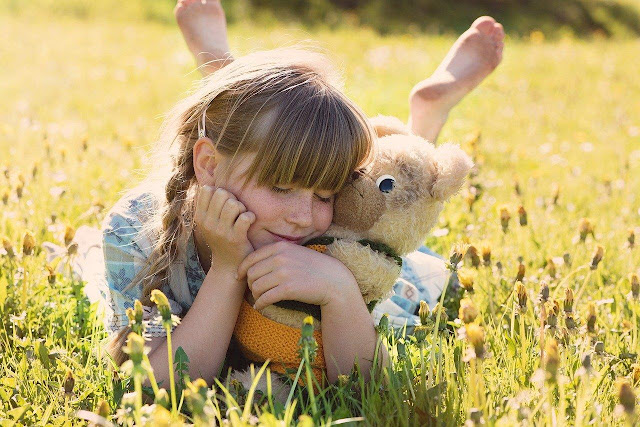 A girl with a teddy bear lying in the grass