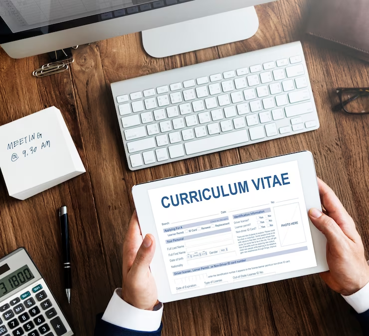 A laptop with a blank screen displaying a student CV layout illustration, surrounded by writing tools.