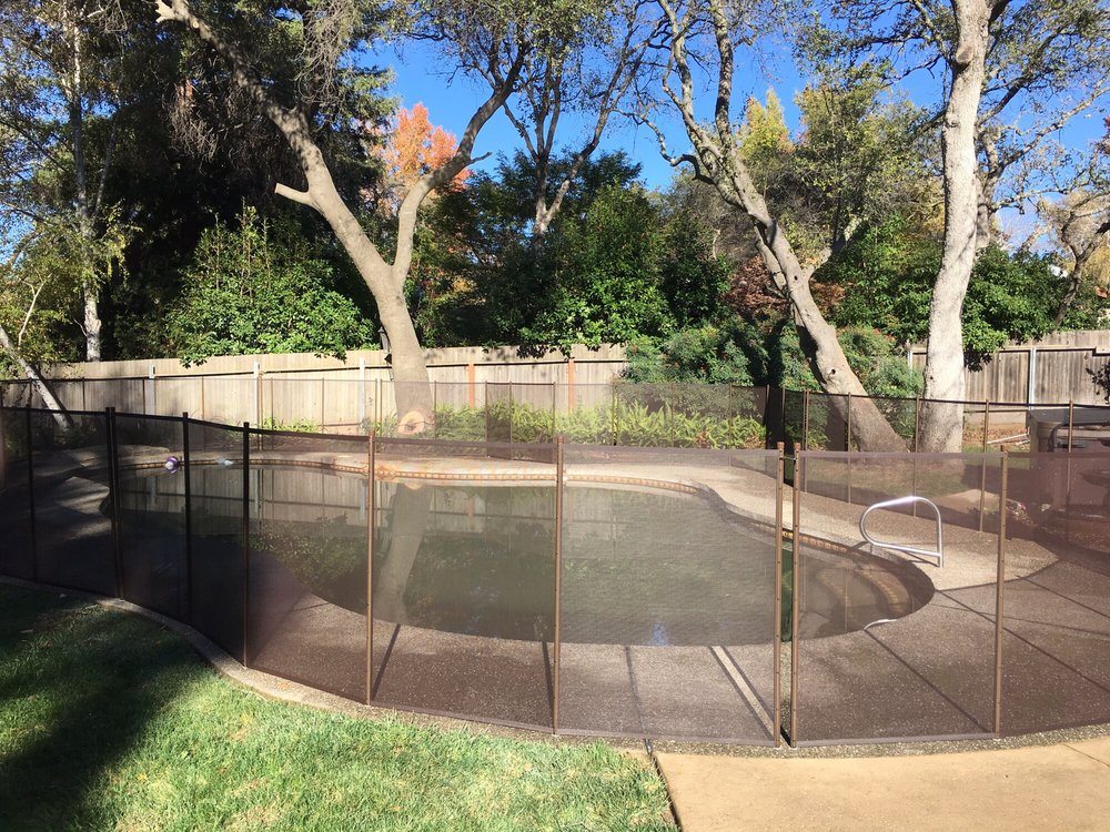 Brown mesh removable pool fence installed around a backyard swimming pool