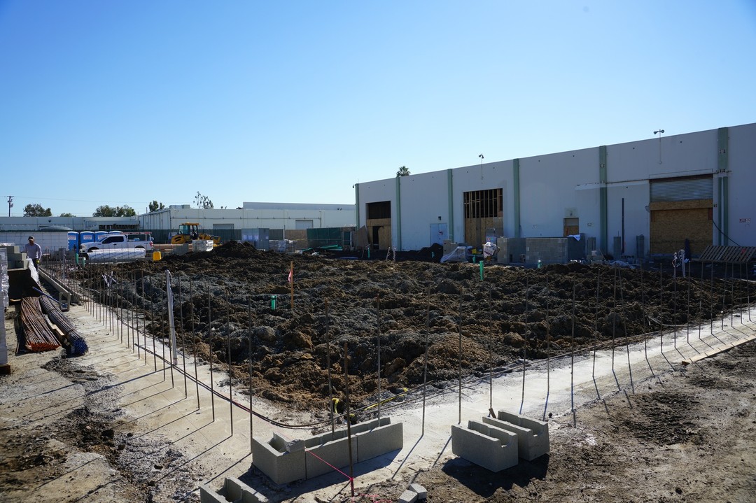 Picture depicting the construction site of the New Homeless Navigation Center during the day. An empty lot is in the foreground with a chain-link fence surrounding it. 