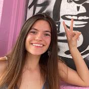 A young girl with long brown hair smiles at the camera while posing the peace sign with her fingers.