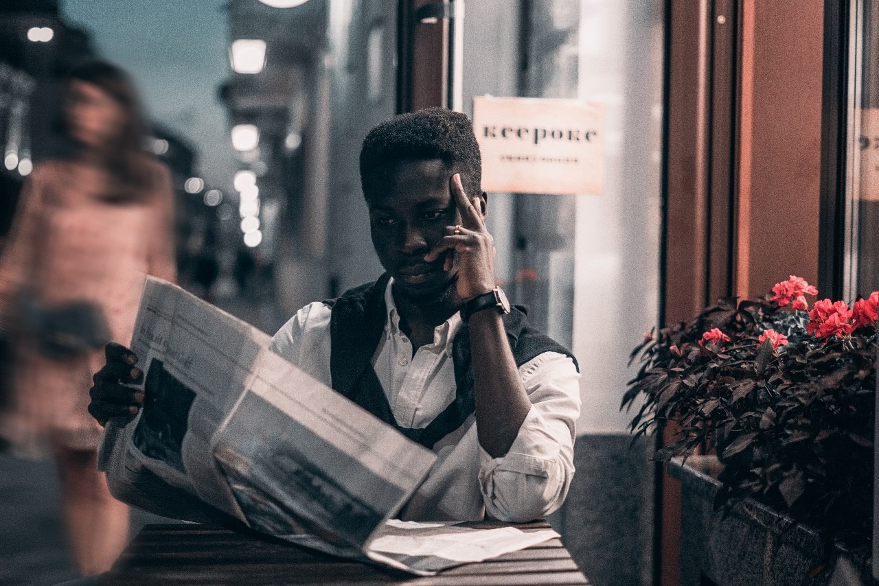 Man reading a newspaper at an outside table at a cafe while wearing a watch