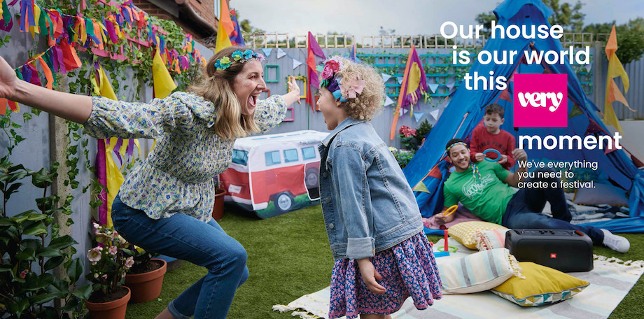 Tearsheet of a family in a backyard that is decorated with brightly colored bunting, a tent, a picnic blanket, and throw pillows. The backyard is decorated as if it is a music festival and the people are wearing flower crowns and festival-like clothing.