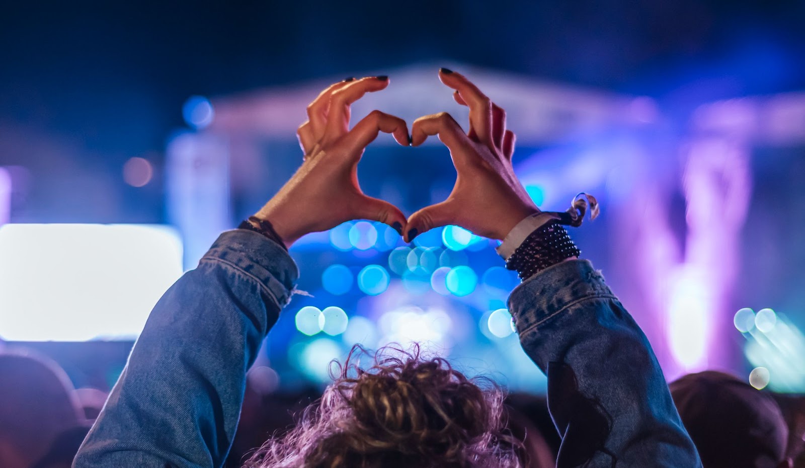 Fan at a music concert with hands raised and fingers in the shape of a heart. 