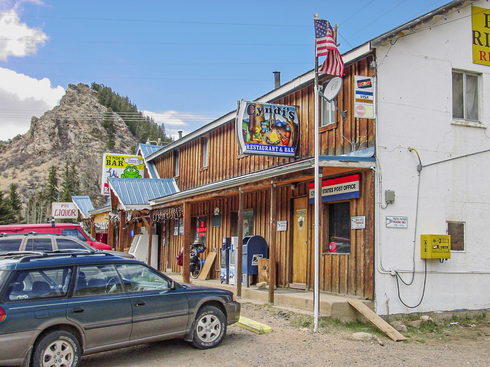 A rural post office and bar with a rocky peak in the background. 