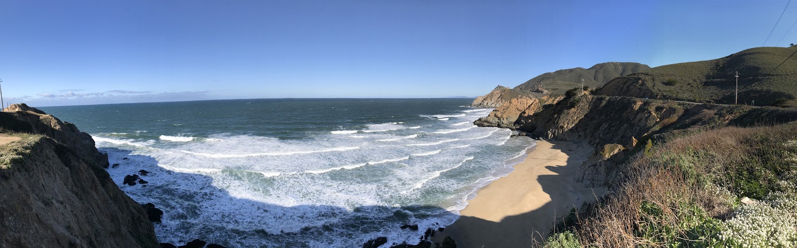 panoramic view beautiful secluded california sandy beach and wavy ocean surrounded by green hills on a clear day. See the beautiful coast of California during a california road trip