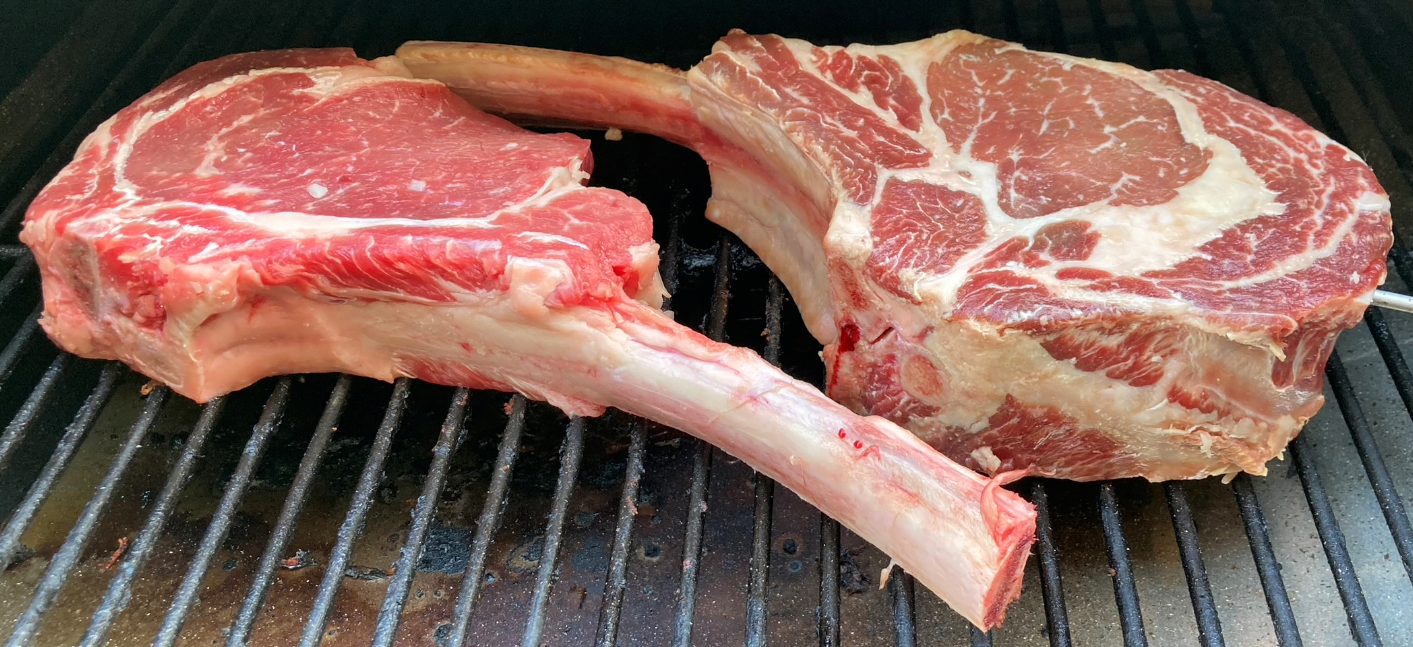 two thick cut tomahawk steaks on a grill