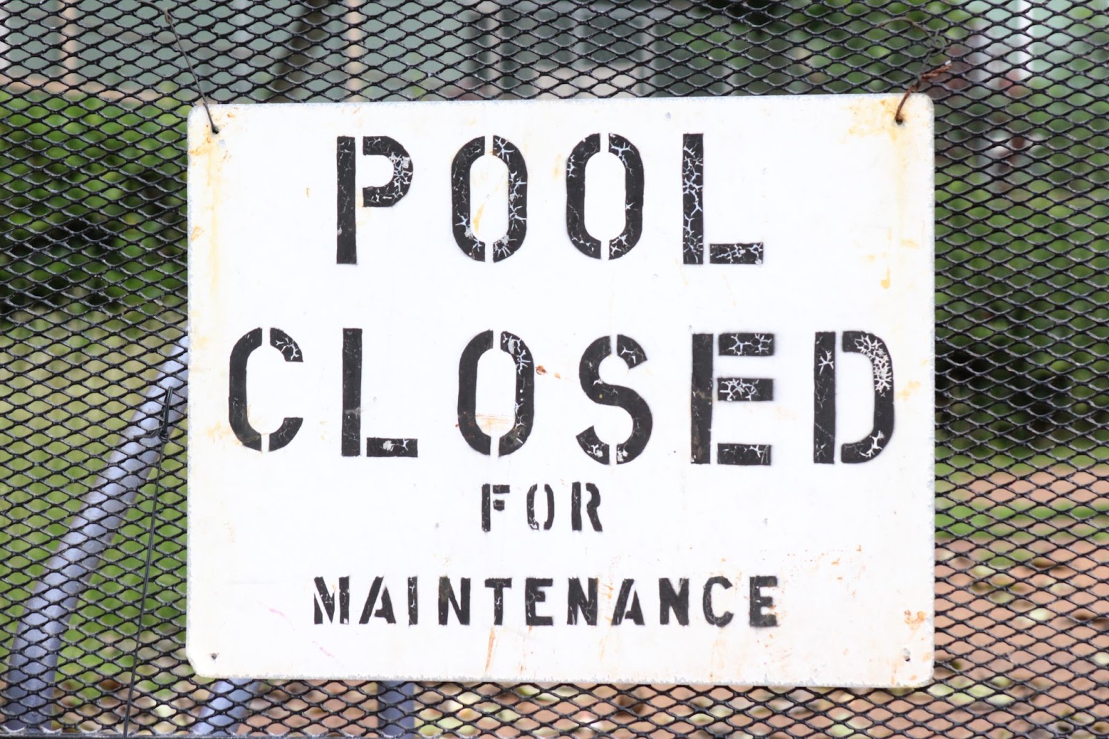 A sign saying the 'Pool is closed for maintenance' as a pool service business cleans the area