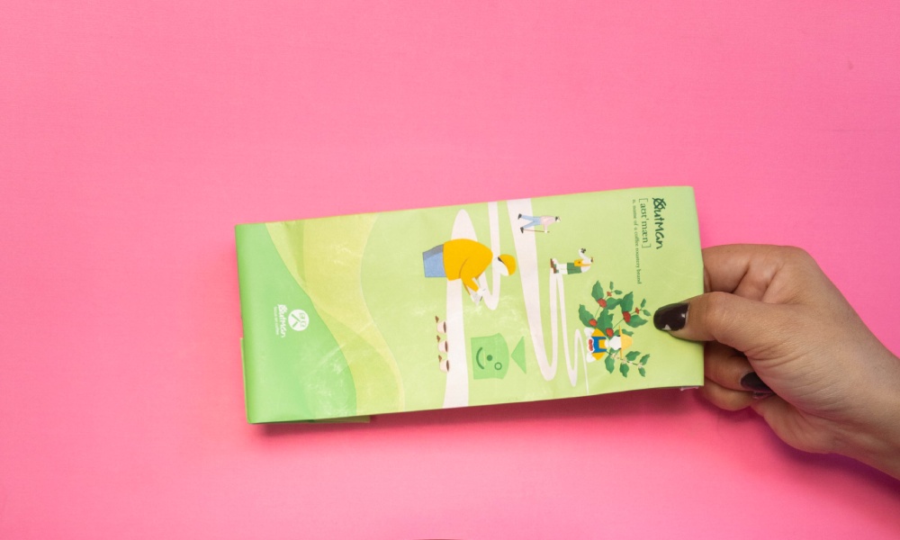Caucasian female hand holds green multilayer kraft paper coffee pouch on bright pink background. 