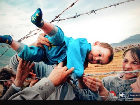 La foto ganadora del Pulitzer del año 2000, que muestra cómo un kosovar refugiado en Agim pasa Shala pasa a través de una cerca de alambre de púas a las manos de sus abuelos, en un campamento dirigido por Emiratos Árabes Unidos en Kukes, Albania. Los miembros de la familia Shala fueron reunidos aquí después de huir del conflicto en Kosovo.

