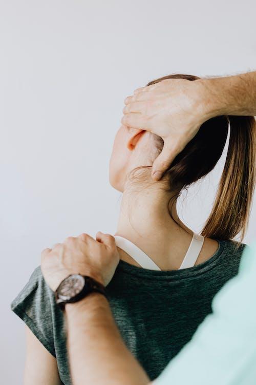 Free Back view of crop faceless chiropractor in wristwatch stretching neck of unrecognizable female patient during medical examination in doctor office in clinic Stock Photo