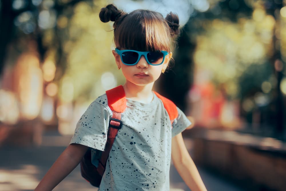 Girl wearing stylish outfit with sunglasses, orange backpack, and earrings posing for camera 