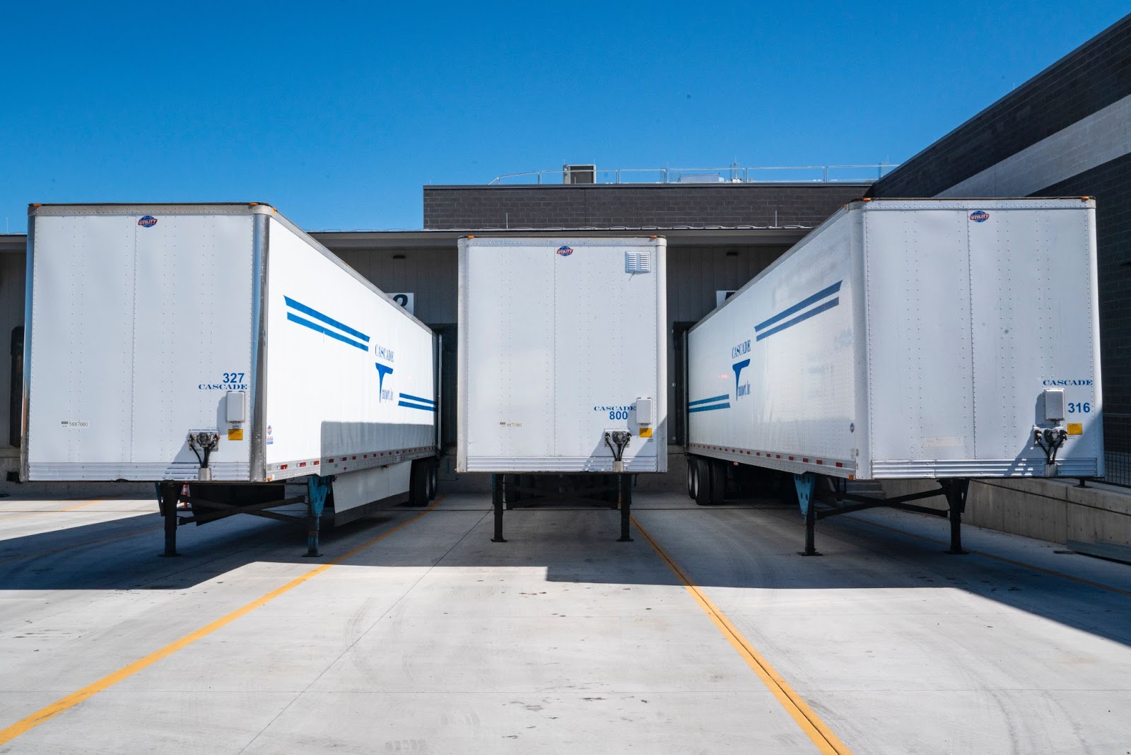 Three white semi-trailers sitting in a warehouse delivery lot.