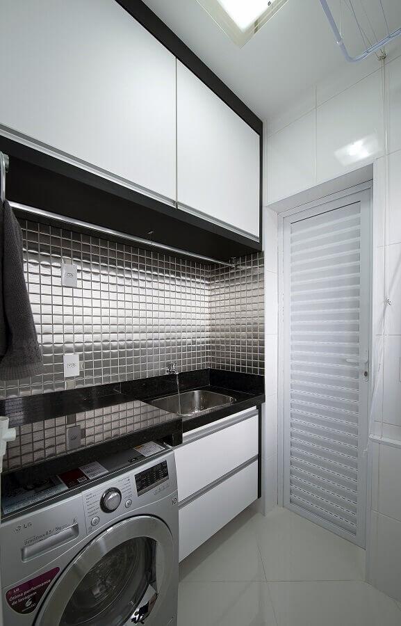 Lavanderia com pastilhas metalizadas na cor preta, pia e bancada de mármore preto, lavadora de inox e piso porcelanato branco.