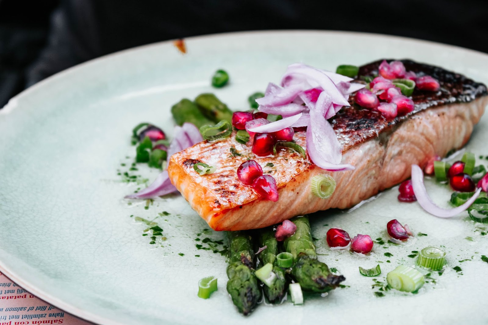 salmon with red onion, pomegranate seeds, and asparagus, on a white plate, highlighting kelowna restaurants to check out while on a babymoon getaway