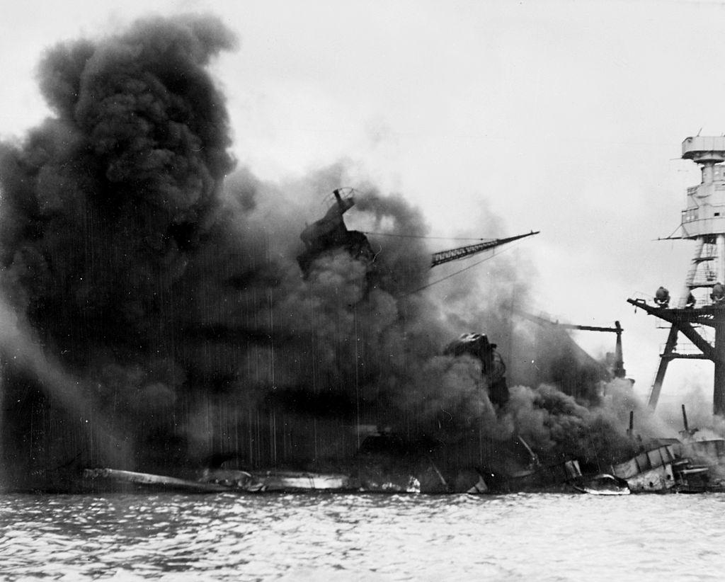 The US battleship Arizona in flames, sinking into Pearl Harbor.