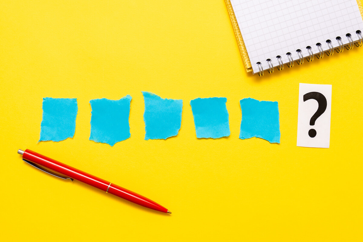 Notepad, red pen, blue pieces of paper and a question mark