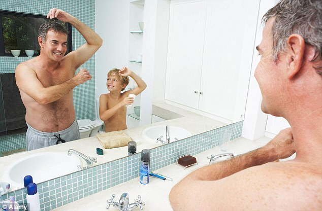 A man and a younger boy applying deodorant while looking in a mirror.