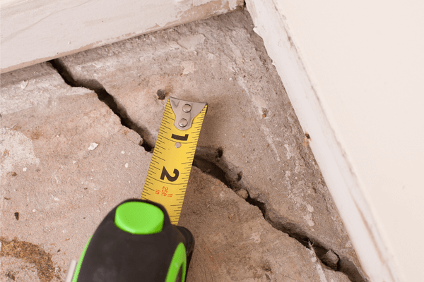 residential floor crack with a measuring tape showing the width of the crack