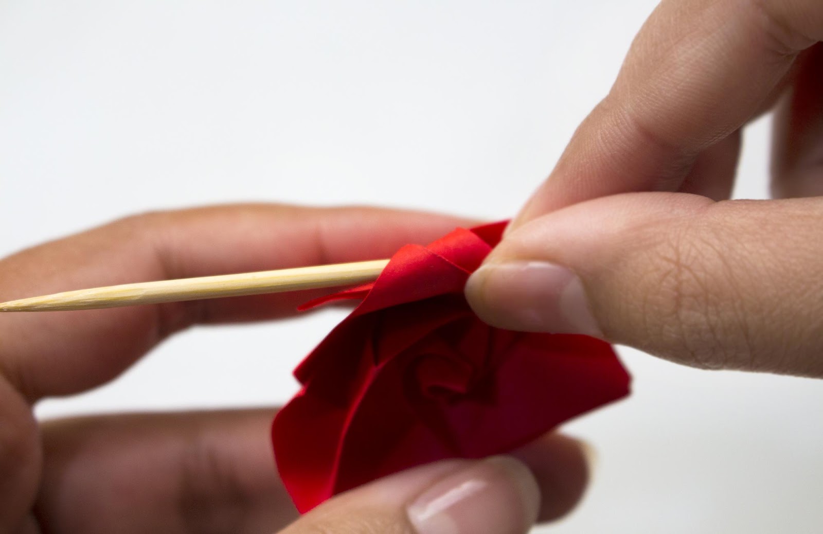 A wooden chopstick is used to curl the edges of an origami flower petal
