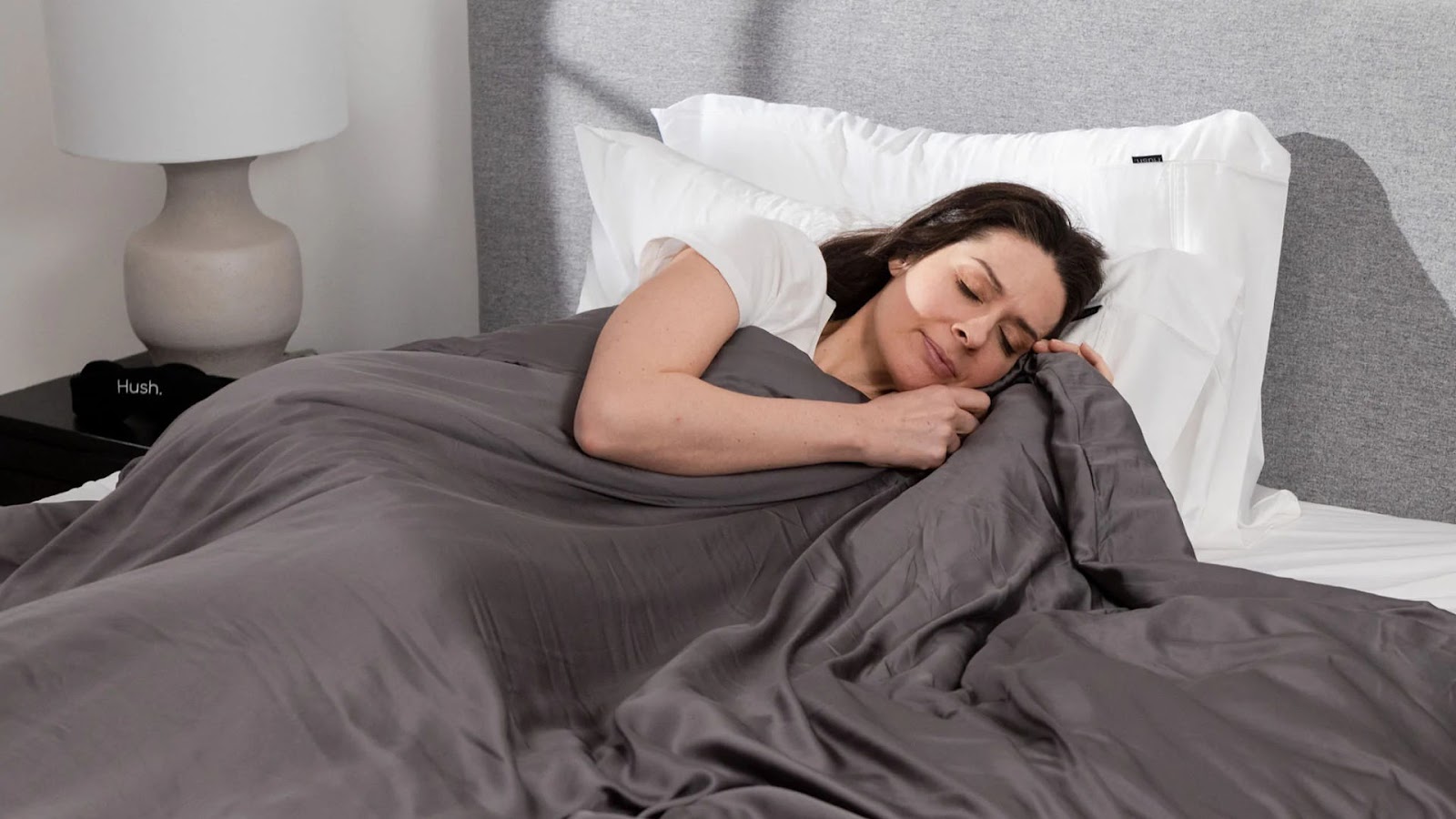 A woman snuggling up in bed with a set of Hush sheets.