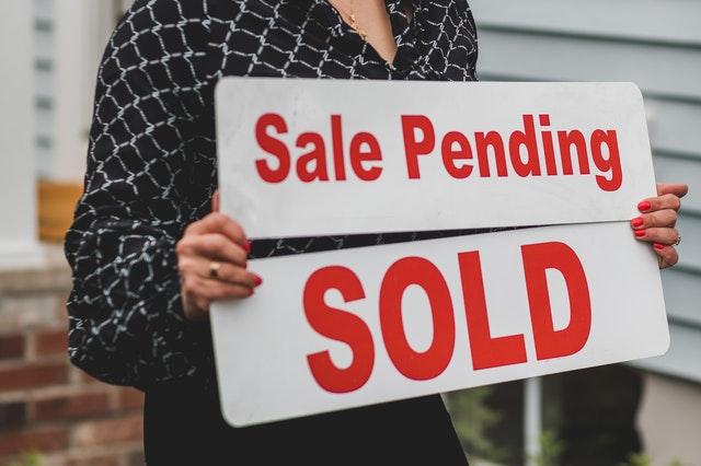 A woman holding two signs saying SALE PENDING and Sold.