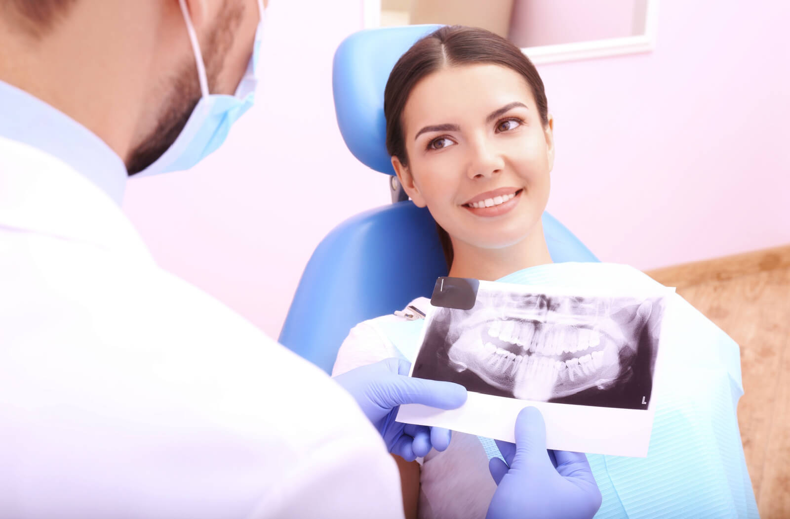 A male dentist explaining a dental implant procedure to a woman while holding a dental x-ray image.