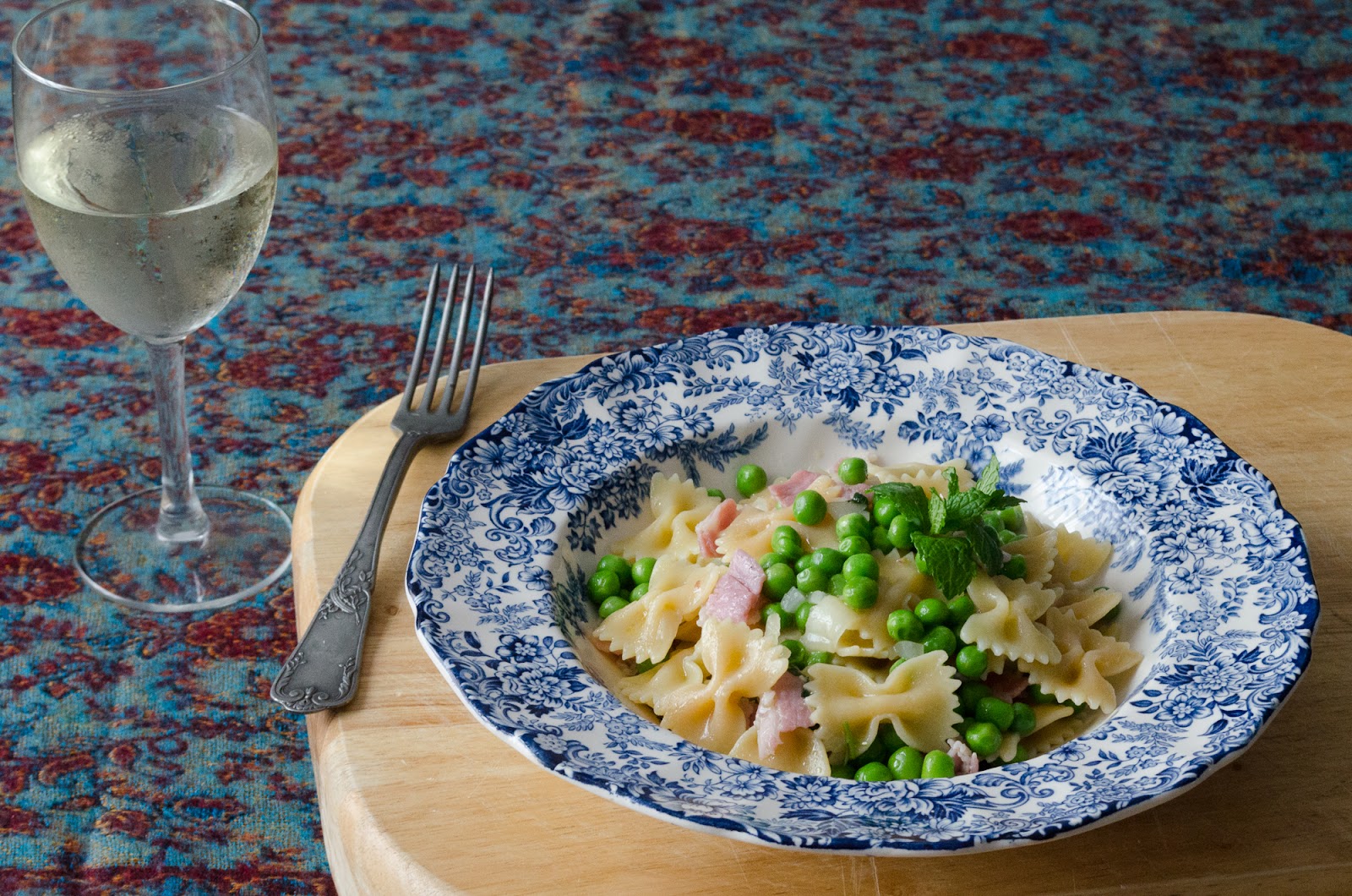 A serving of pancetta pasta with peas and a cold glass of white wine