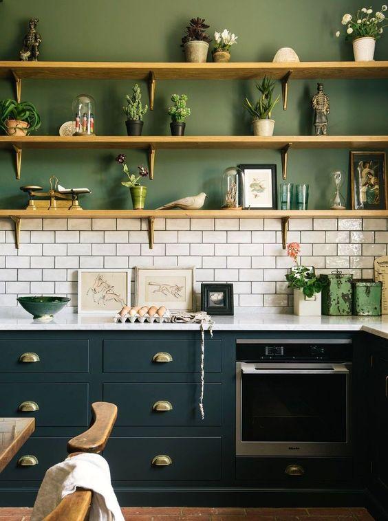 Cozinha em estilo industrial com armário azul com bancada branca, parede de fundo com meia parede inferior revestida de azulejo do metro branco e outra metade pintada de verde com prateleiras de madeira com objetos decorativos e piso de cera.