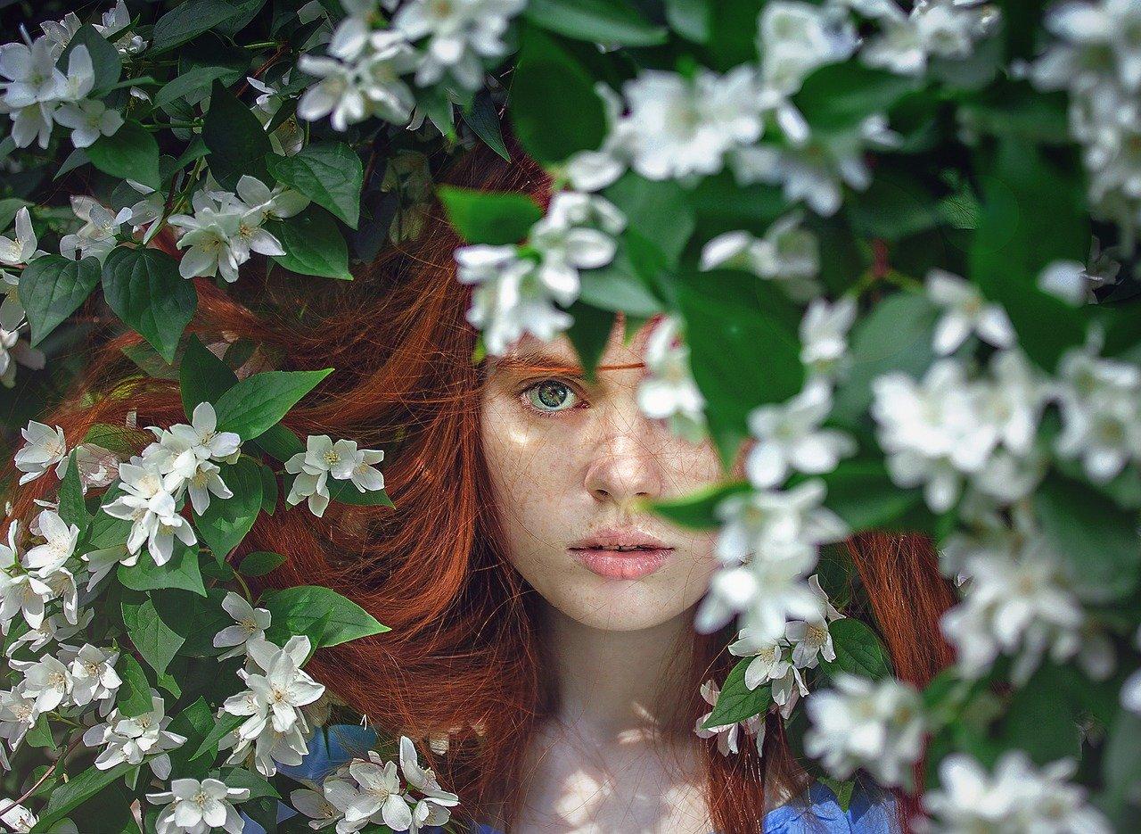 woman with red hair peaking through flowers