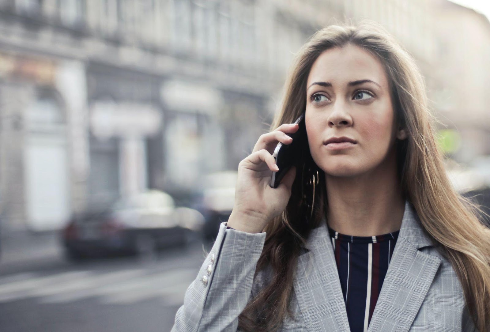 A woman in a gray suit on the street talking to someone over her phone 
