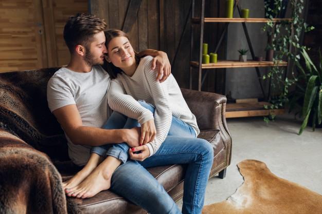 Young smiling couple sitting on couch at home in casual outfit Free Photo