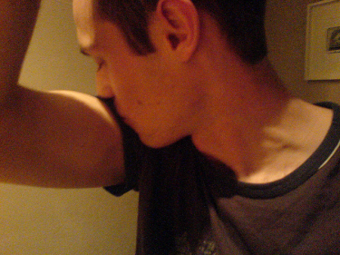 A close-up photograph of a male-presenting individual turning his head to smell the outer part of his bicep. 