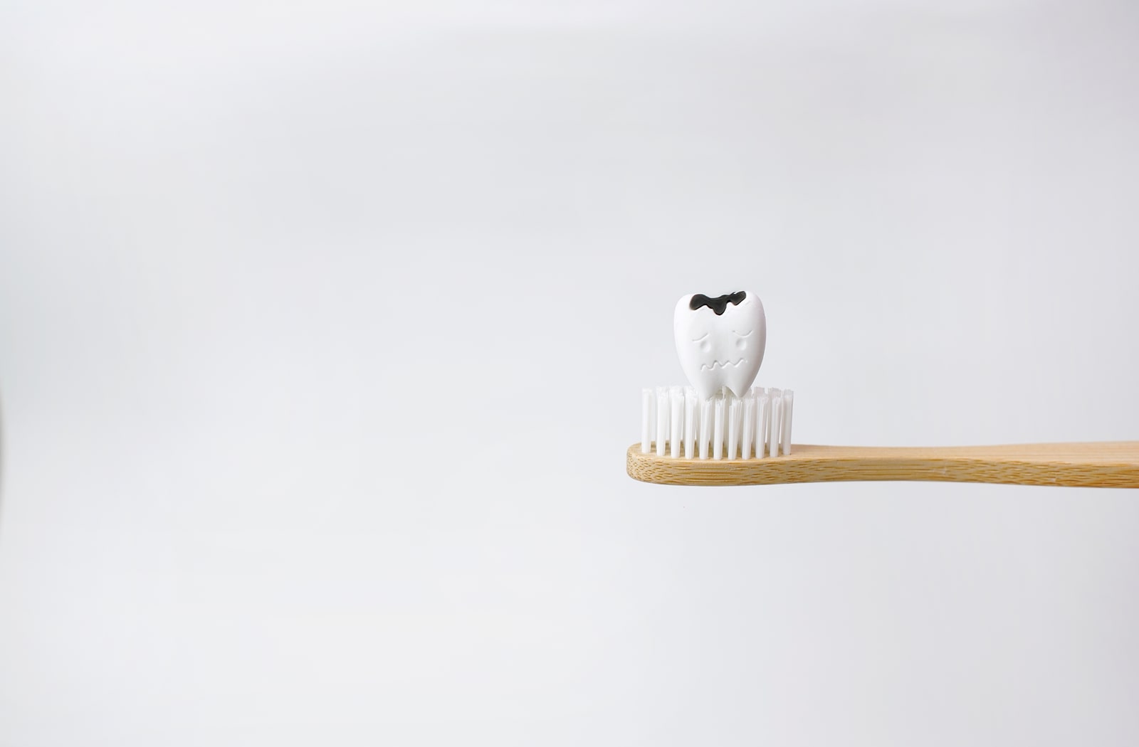 A plastic tooth with a cavity on it, sitting on top of a wooden toothbrush