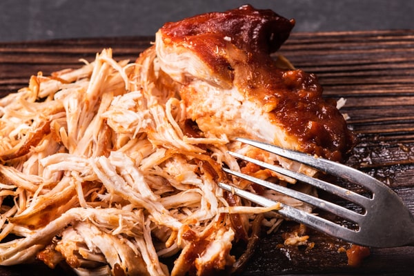 A pulled chicken with a fork and placed on a wooden board