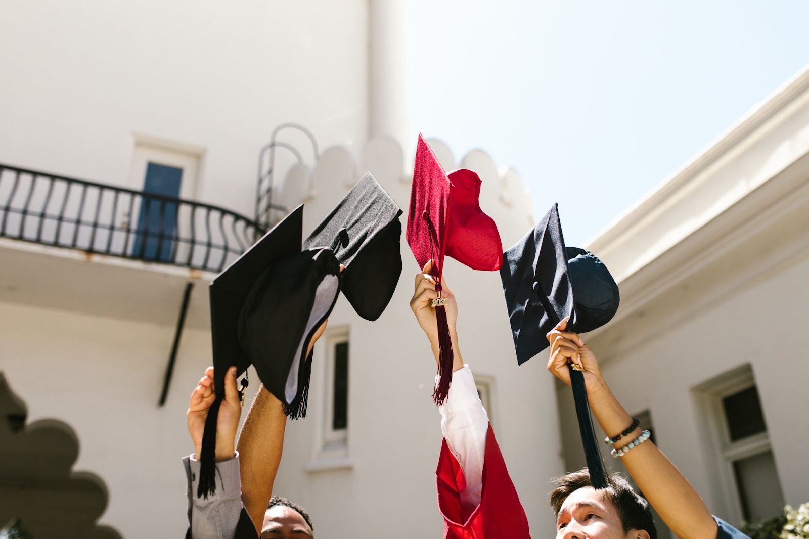 multicultural group of people holding graduation caps in the air