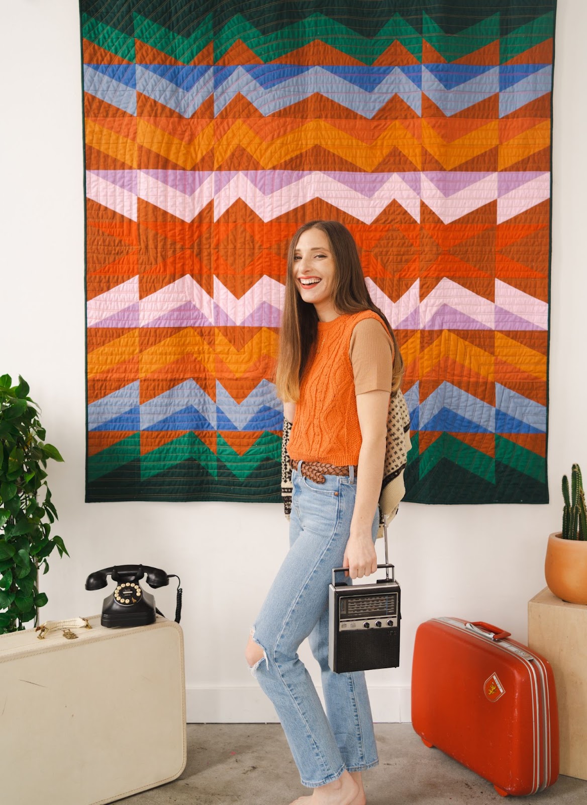 Taylor Krz standing in front of Rocky Coast Quilt holding vintage stereo and sweater