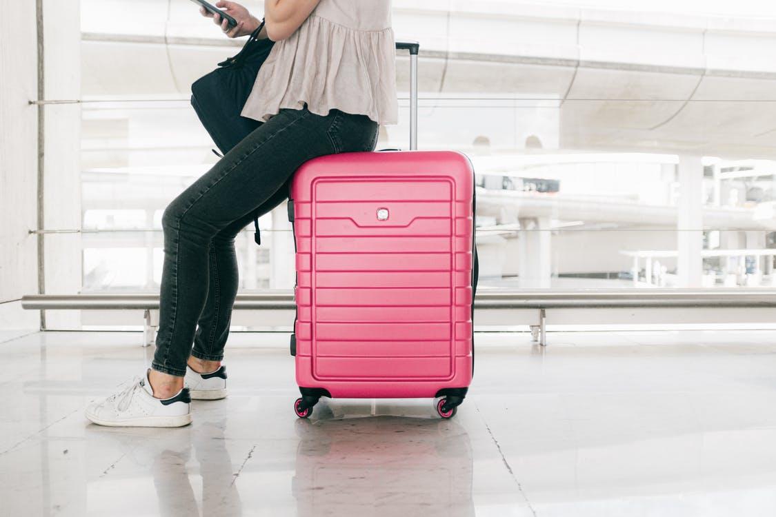 Woman In White Top And Denim Jeans Sitting  On Red Luggage Bag