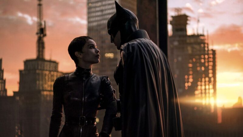 Catwoman and Batman talk as the sun sets in the city behind them