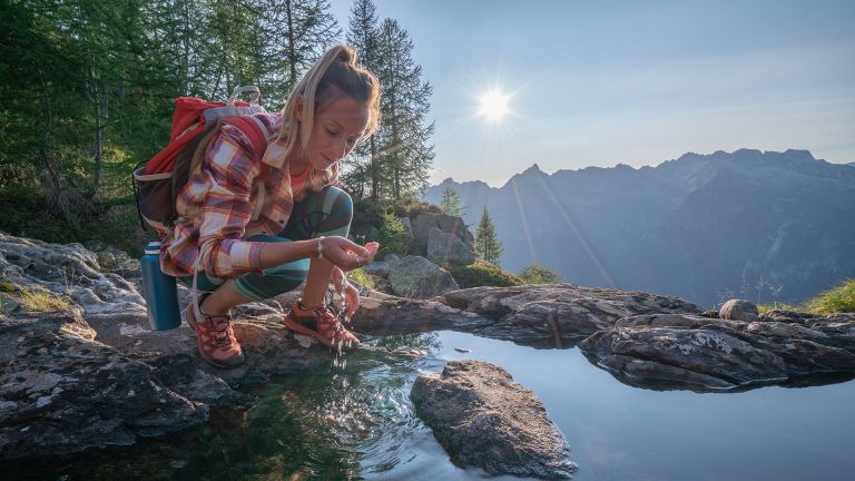 woman scooping mountain water from a pool