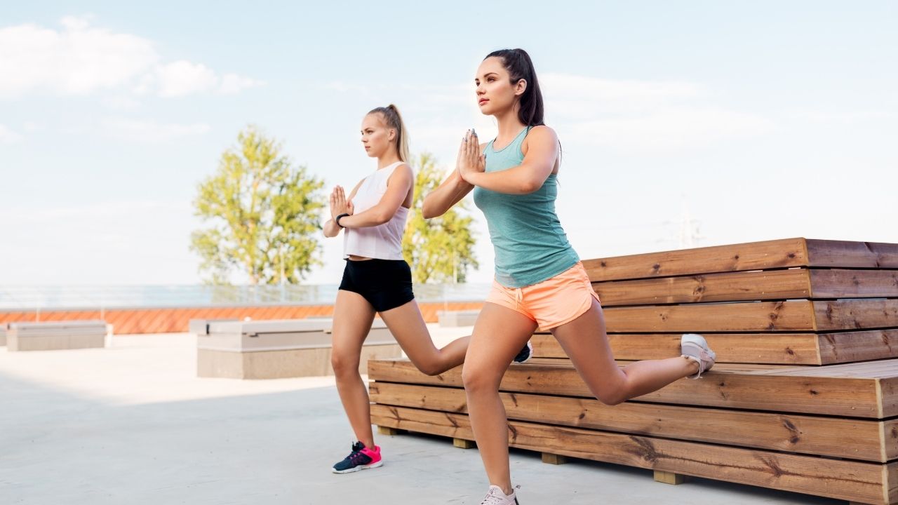 Two women perform bodyweight rear-foot elevated splits squats.