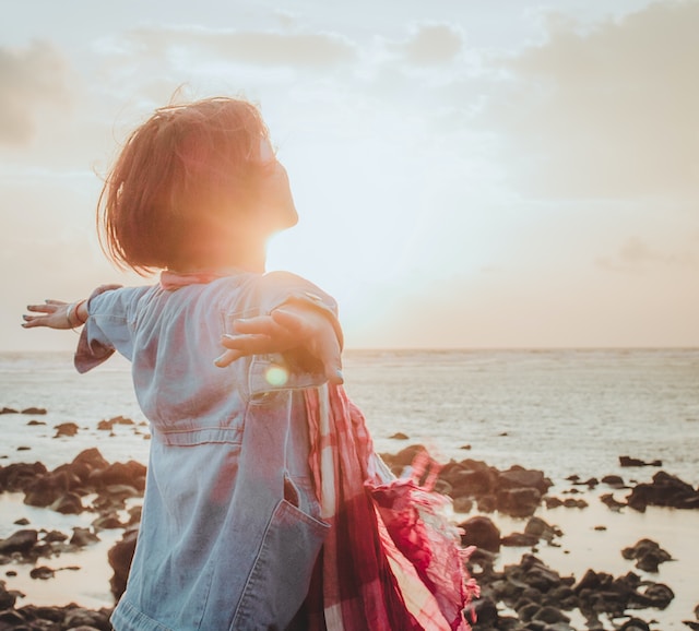 Woman with arms spread feeling alive and inspired by the ocean and sunset