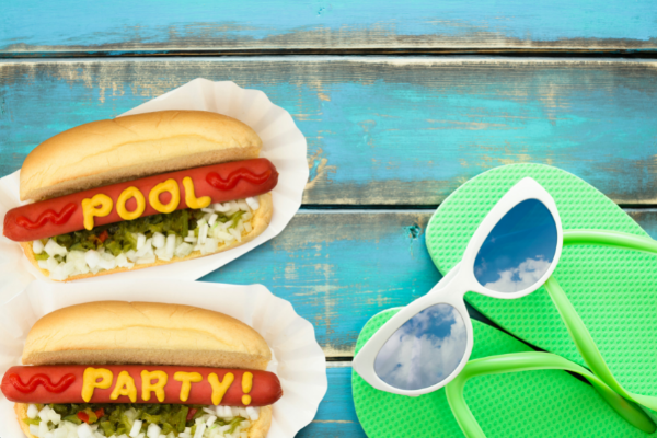 dressed hot dogs spelling 'pool party' in condiments next to flip flops and sunglasses