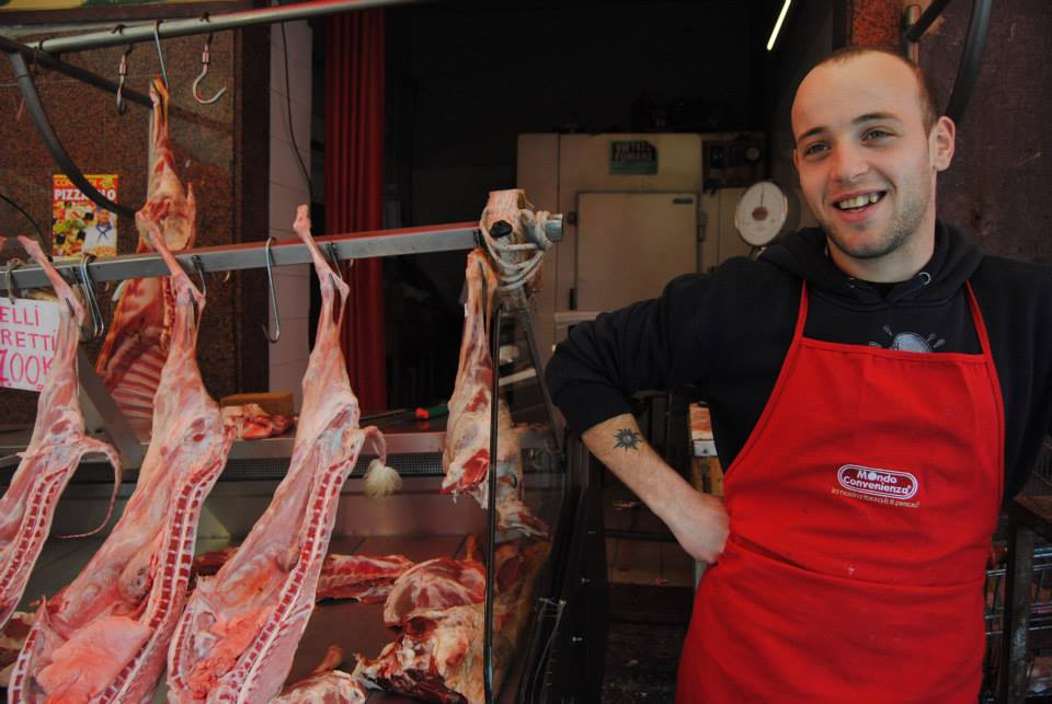 A vendor stands near the meat he's selling with a smile on his face.