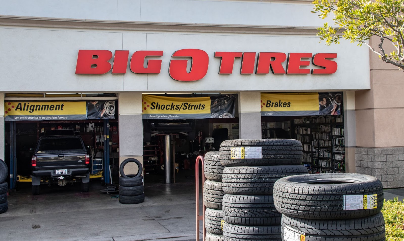 A picture of a Big-O-Tires store with tires outside and people working inside the shop.