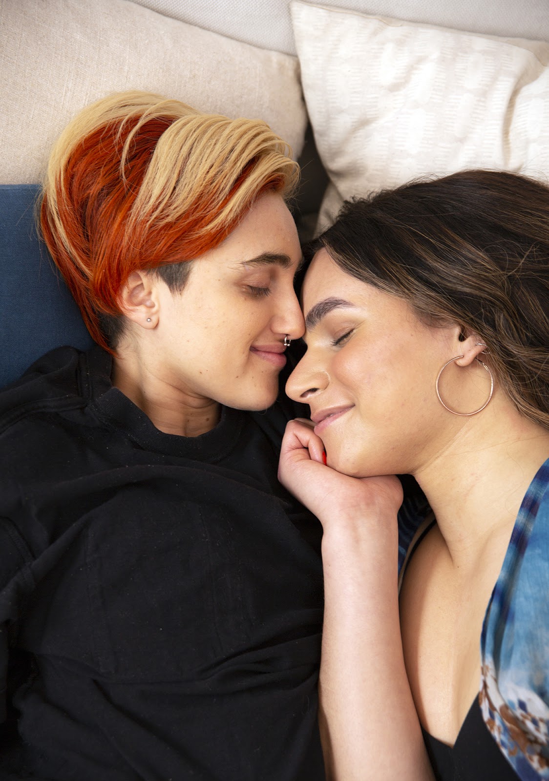 Two persons next to each other in bed, with their foreheads touching.