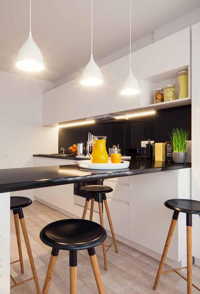 Cozinha com armários brancos, bancadas pretas, banquetas de madeira com assento preto, parede da pia peta, luminárias pendentes brancas e piso de madeira clara.