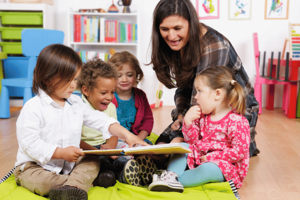 Group of preschool children sitting on the floor with their teacher reading a picture book.